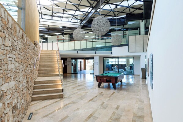 A spacious lobby with a pool table, a staircase, and a high ceiling with hanging spherical light fixtures.