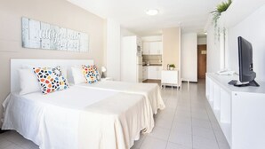 Une chambre d’hôtel avec deux lits, un bureau, une télévision et, au fond, une petite cuisine.