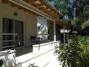 A covered outdoor area with a railing, a bench, and a door leading to a building. - Soller Garden (Sóller)