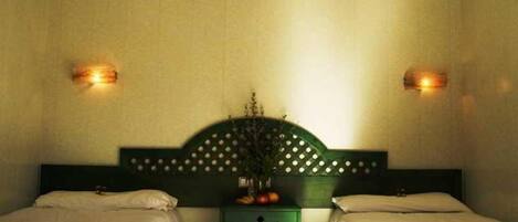 Ein Hotelzimmer mit zwei Einzelbetten, einem grünen Nachttisch mit Blumenvase und Wandleuchten.