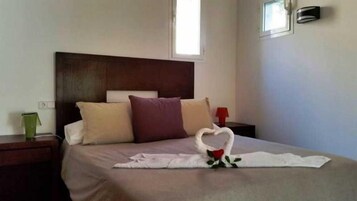 A hotel room with a bed, pillows, a nightstand, a lamp, and a heart-shaped towel decoration.