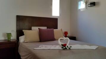 Une chambre d’hôtel avec un lit, une table de chevet, un vase vert et une décoration en forme de cœur faite avec une serviette.