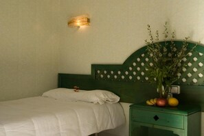 A bed with white bedding, a green headboard, a nightstand with a vase of flowers and fruit, and a wall-mounted light fixture. - Soller Garden (Sóller)