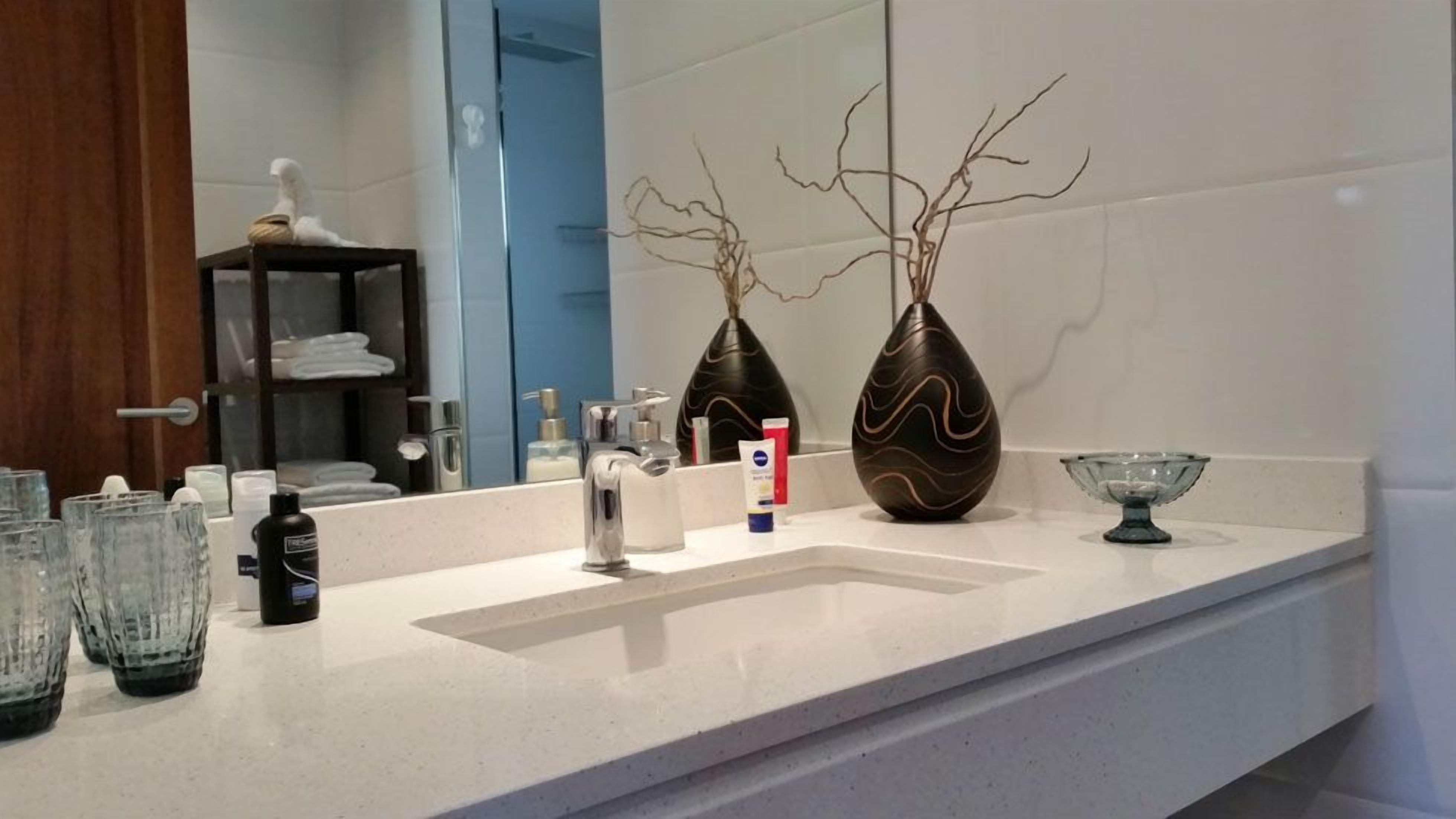 Een badkamer met een witte wasbak, twee decoratieve vazen, een glazen schaal en toiletartikelen op het aanrecht.
