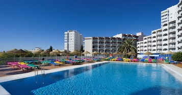 A swimming pool with colorful lounge chairs and umbrellas, surrounded by multi-story buildings with balconies.