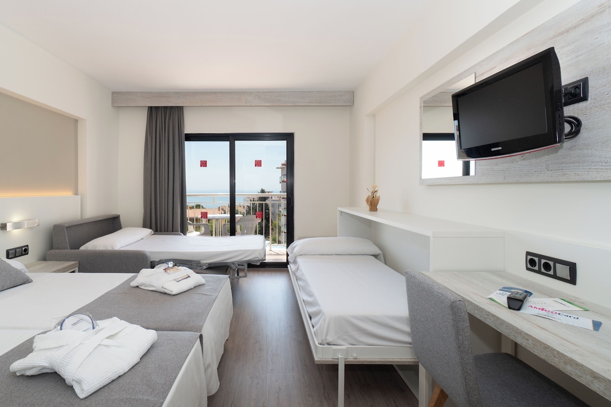 A hotel room with two single beds, a TV, a small table with a vase, and a balcony with a view.