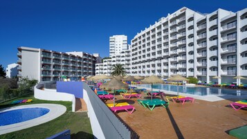 A resort with multiple white buildings, a swimming pool, and colorful lounge chairs.