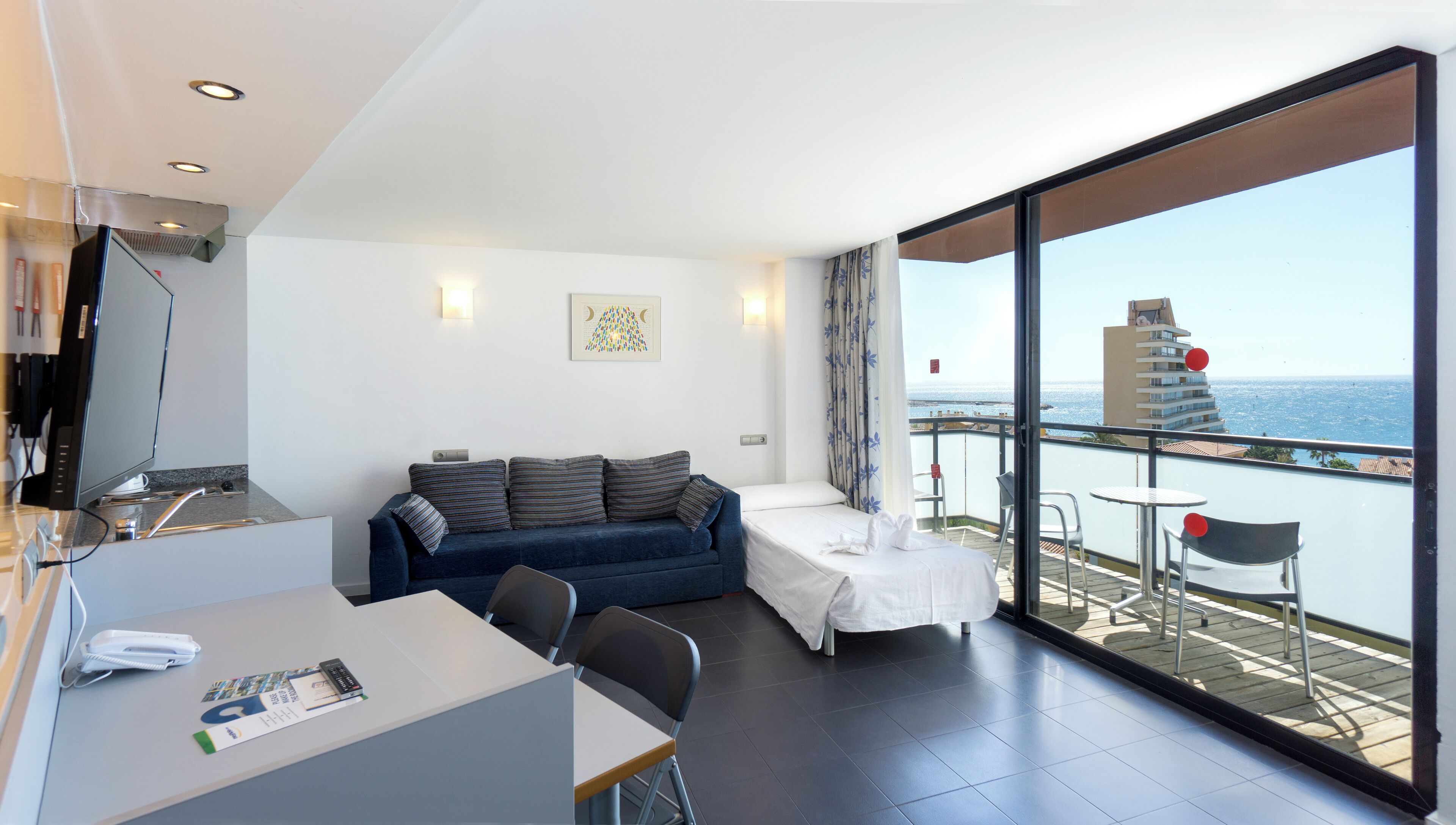 A modern room with a sofa, a small table, and a balcony with a view of the sea.