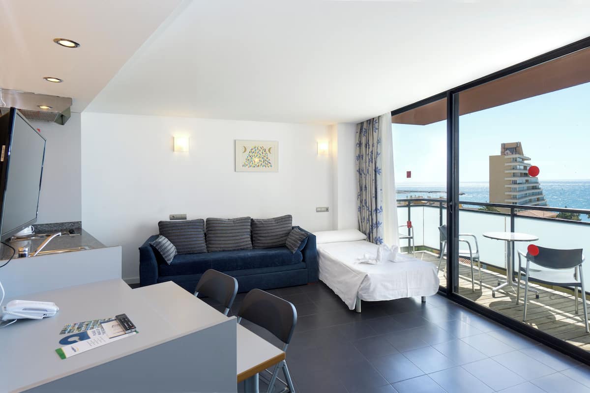 A modern room with a sofa, a small table, and a balcony with a view of the sea.