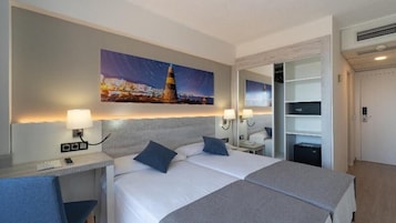 A hotel room with a bed, bedside tables, lamps, a painting of a lighthouse, and a wardrobe.