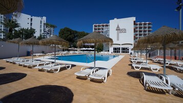 A hotel pool area with sun loungers, umbrellas, and a clear blue pool.