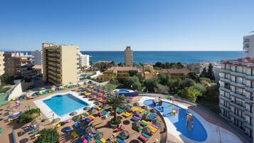 A resort with a pool area, multiple buildings, and a view of the sea.