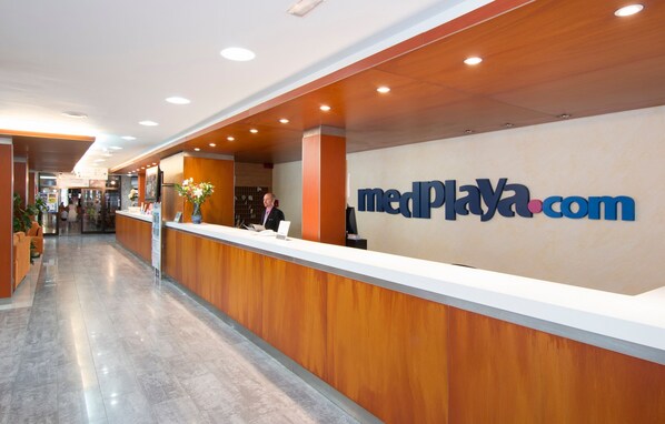 Zona de recepción con un mostrador de madera, un cartel que dice "medPlaya.com" y una puerta de cristal que da al interior.