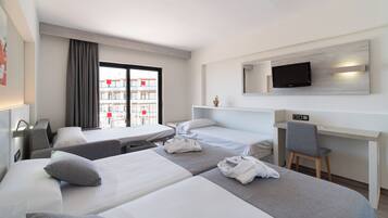 Habitación de hotel con dos camas, un escritorio, una silla, un televisor y ventana con vistas a edificios.