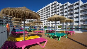 Zona de piscina en un resort con sillas de descanso coloridas y sombrillas de paja.