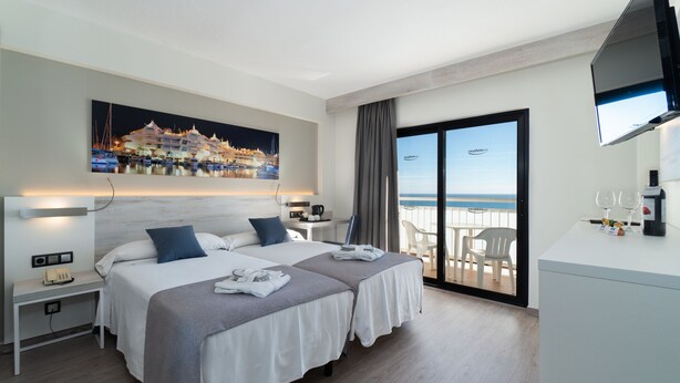 A hotel room with two beds, a desk, a chair, a TV, and a balcony with a view of the sea. - Medplaya Bali (Benalmádena)