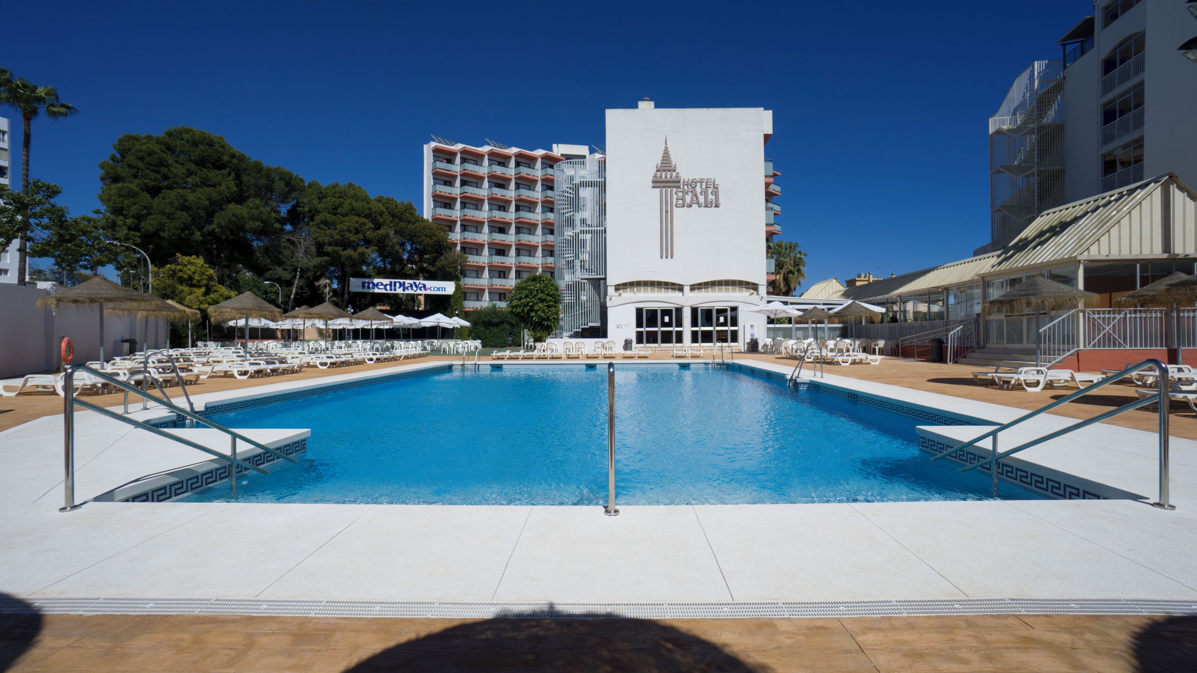 Ein Hotelpoolbereich mit einem klaren, blauen Pool, weißen Liegestühlen und Sonnenschirmen.