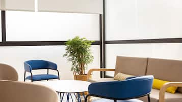 A modern room with a round table, two blue chairs, a beige sofa, and a potted plant.