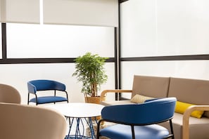 Una habitación moderna con una mesa redonda, dos sillas azules, un sofá color beige y una planta en maceta.