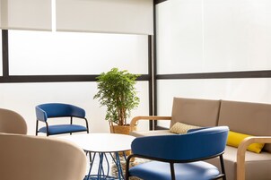 Una habitación moderna con una mesa redonda, dos sillas azules, un sofá color beige y una planta en maceta.
