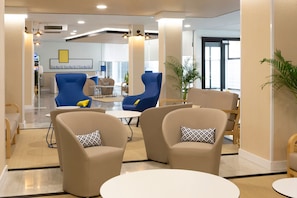 Un vestíbulo moderno con sillones color beige, un sillón azul y una mesita.