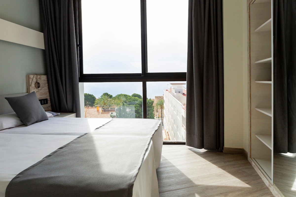 A bedroom with a large bed, a wooden headboard, a view of the city through a large window, and a built-in wardrobe.