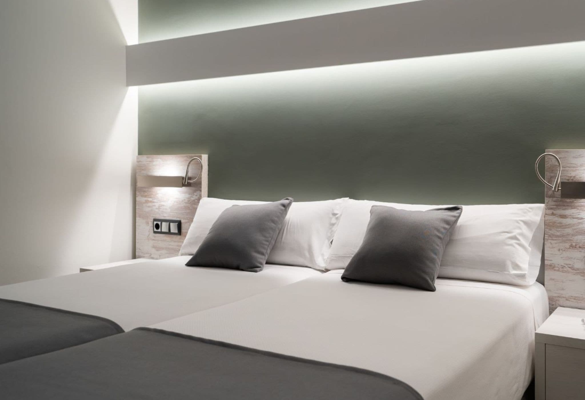 A modern hotel room with a large bed, two bedside tables, and a built-in shelf.