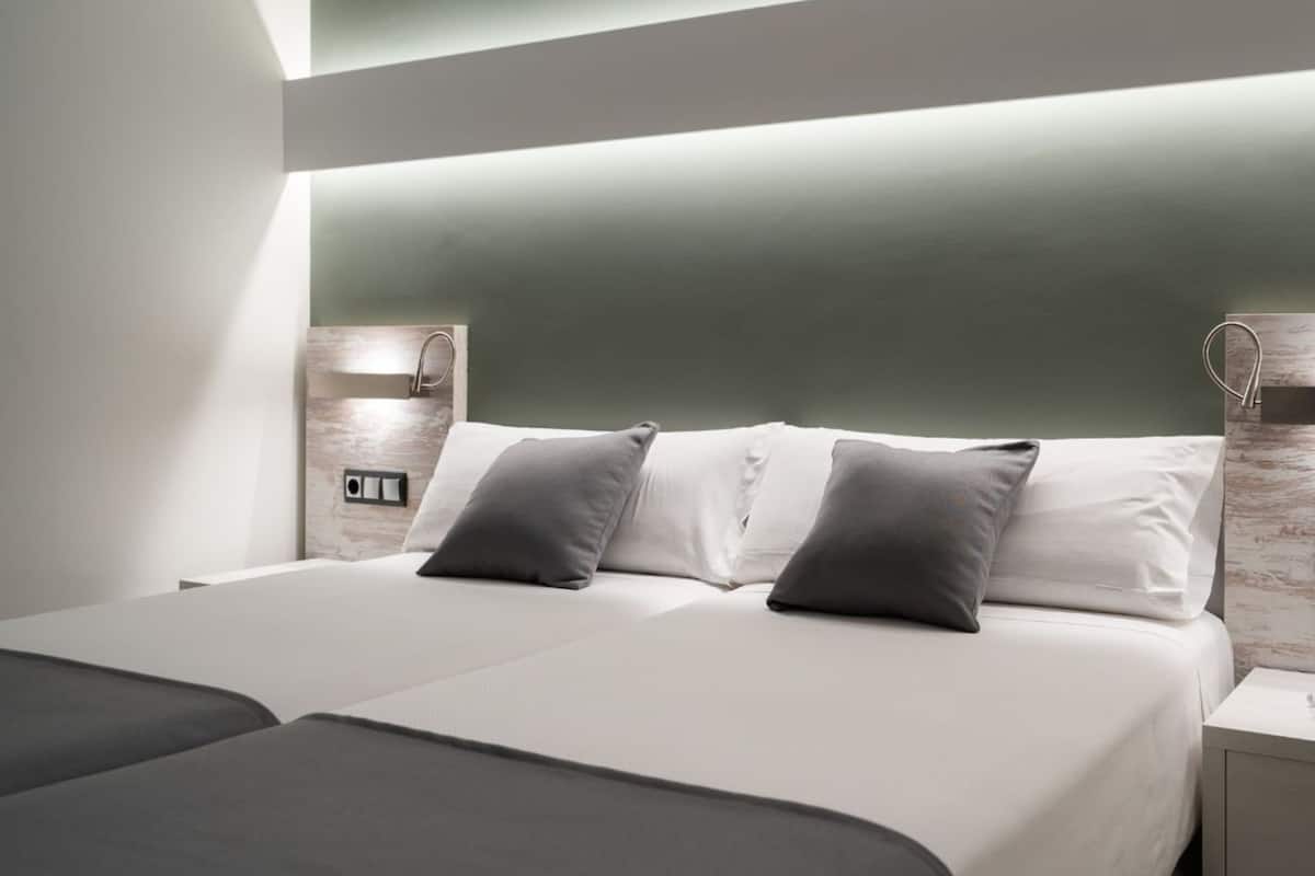 A modern hotel room with a large bed, two bedside tables, and a built-in shelf.