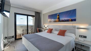Habitación de hotel con cama, escritorio, silla, teléfono y un cuadro de un paisaje urbano.