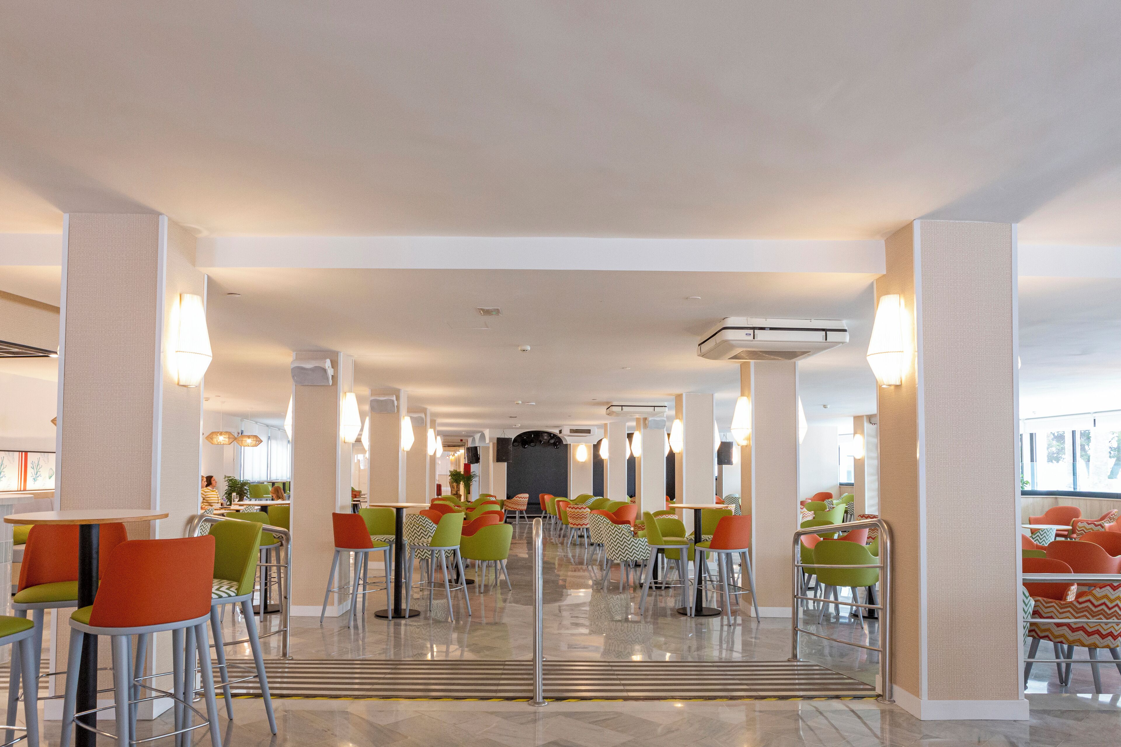 A spacious indoor dining area with multiple tables and chairs, a central walkway, and a view of the outside.
