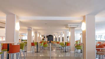 A spacious indoor dining area with multiple tables and chairs, a central walkway, and a view of the outside.