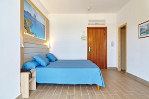 Una habitación de hotel con cama, mesita de noche, un cuadro y una puerta.