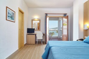Una habitación de hotel con cama, escritorio con computadora, silla, televisor y balcón con vistas.