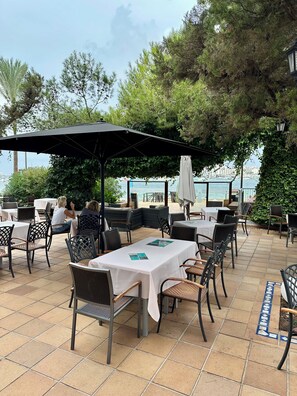 An outdoor seating area with tables and chairs, a covered section, and a view of the sea. - Hotel Ses Savines (Sant Antoni de Portmany)