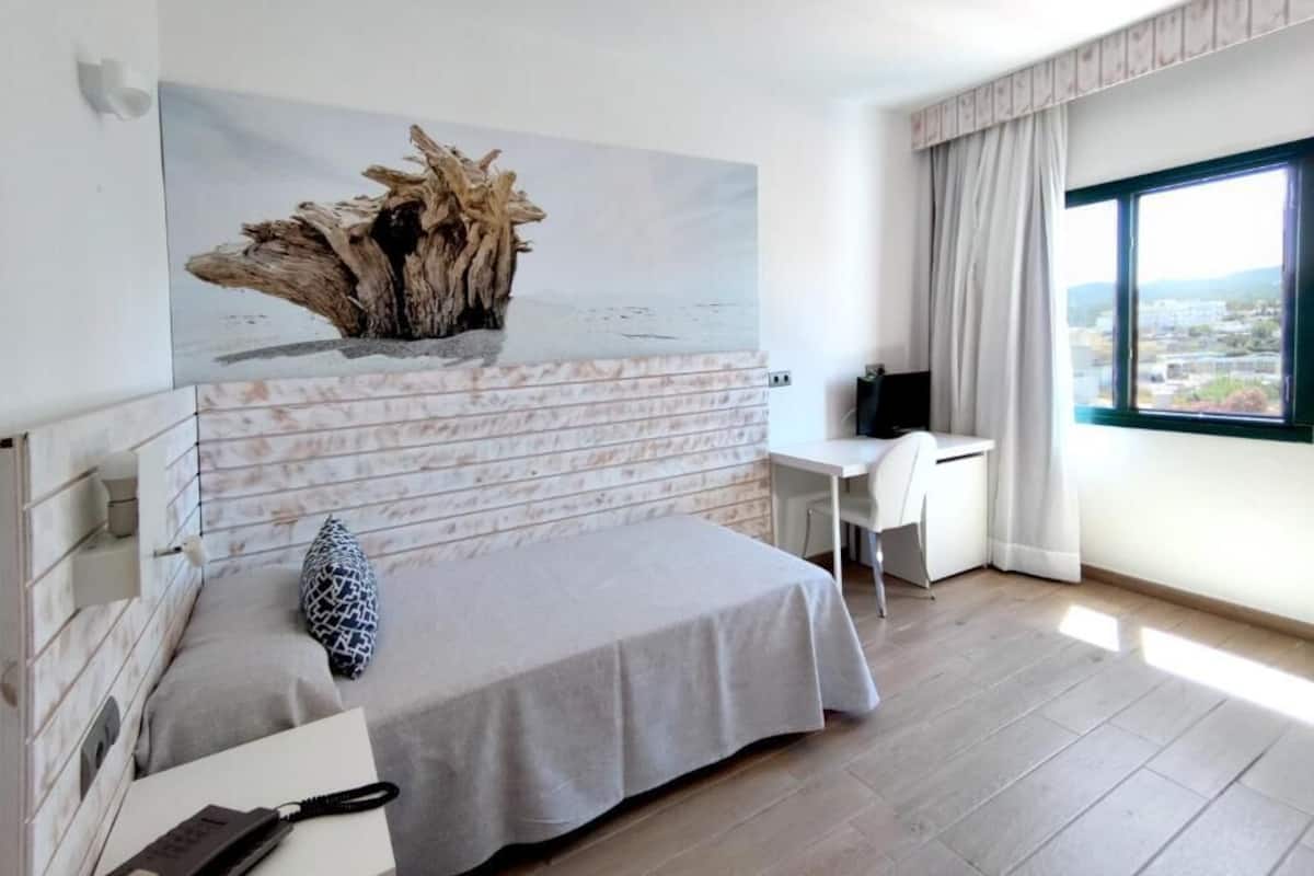 A modern bedroom with a bed, a desk, and a large window.
