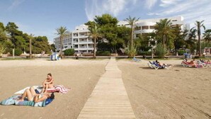 A beach with a wooden walkway leading to a building with multiple balconies, surrounded by palm trees.