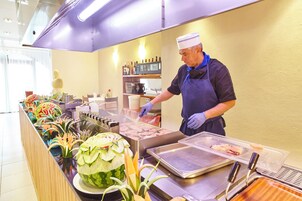 Montaje de buffet con diversos alimentos, incluyendo una sandía tallada en forma decorativa, y una persona sirviendo comida.