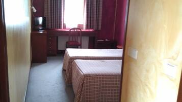 Una camera d'albergo con una scrivania, due letti, una sedia e una finestra con tende.