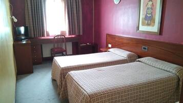 Habitación de hotel con dos camas, un escritorio, una silla y un ventanal con cortinas.