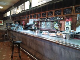 Una zona de bar con taburetes, una barra con varios artículos y menús en una pizarra.