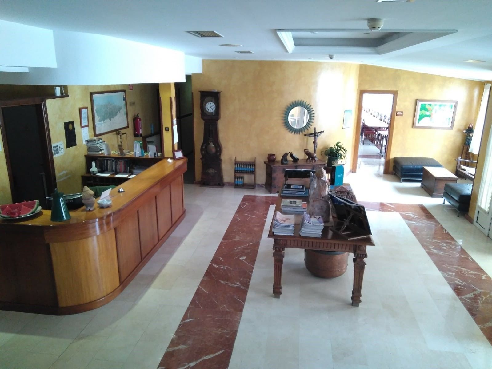 A reception area with a wooden desk, a clock, a mirror, and a cross on the wall.