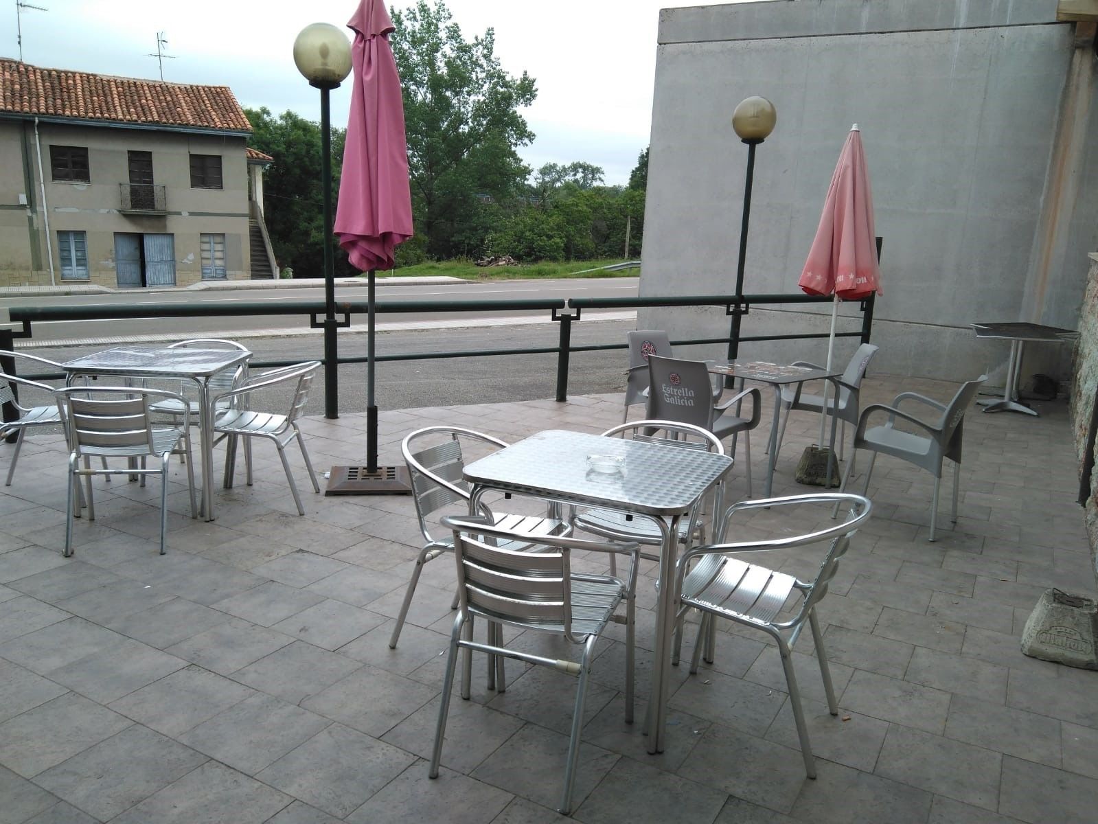 Outdoor patio seating with metal tables and chairs, two pink umbrellas, and a building in the background.
