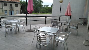 Outdoor patio seating with metal tables and chairs, two pink umbrellas, and a building in the background.