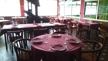 Un restaurante con mesas redondas cubiertas por manteles rojos, sillas de madera y copas de vino vacías.