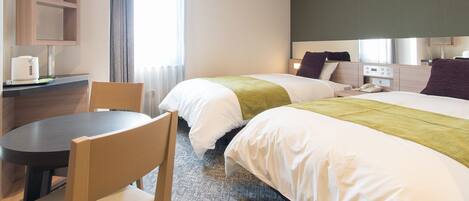 A hotel room with two beds, a desk with a chair, a small table, and a window with curtains.