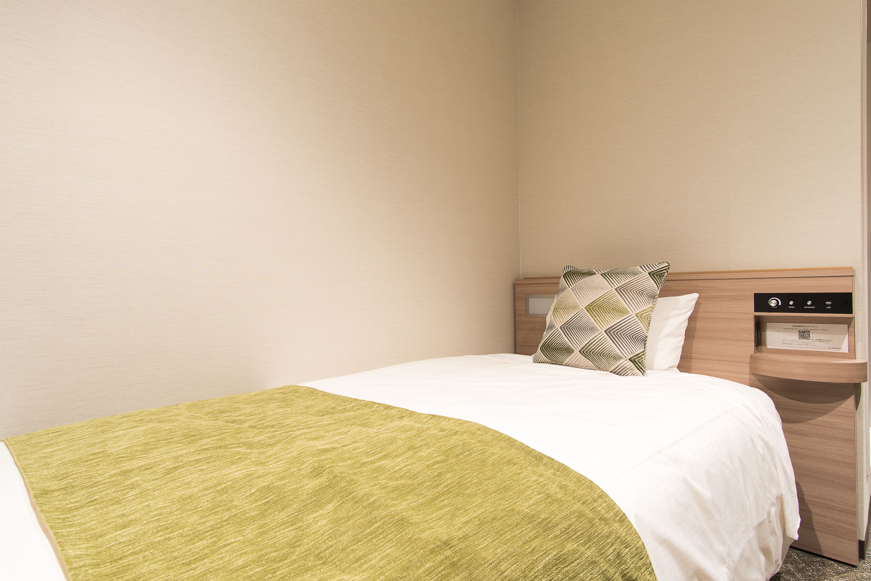 A hotel room with a bed, a nightstand, and a wooden headboard.