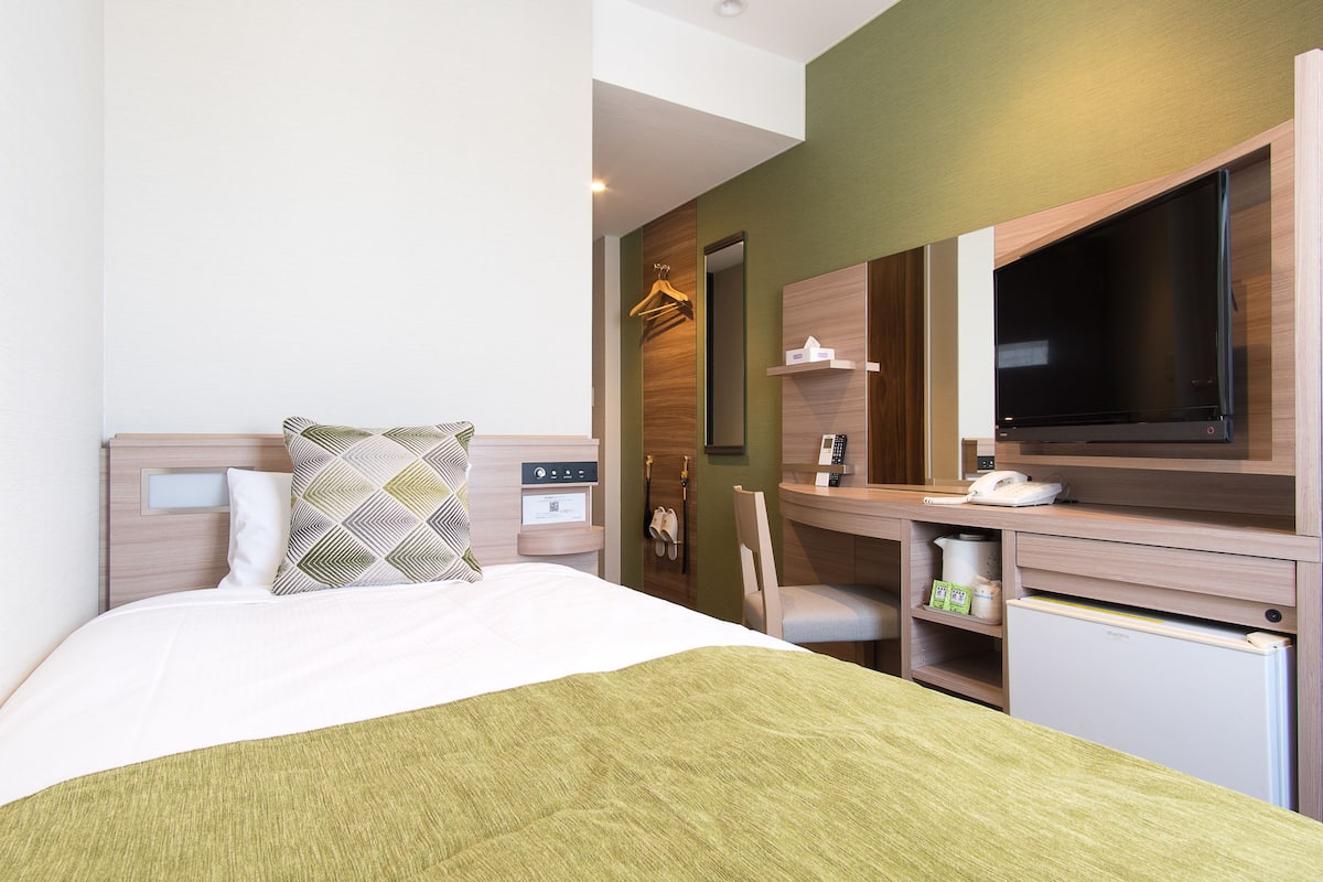 A hotel room with a bed, a desk with a computer, a TV, and a mini-fridge.