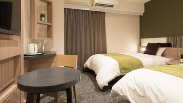 A hotel room with a bed, a desk, a chair, a TV, and an air conditioning unit.