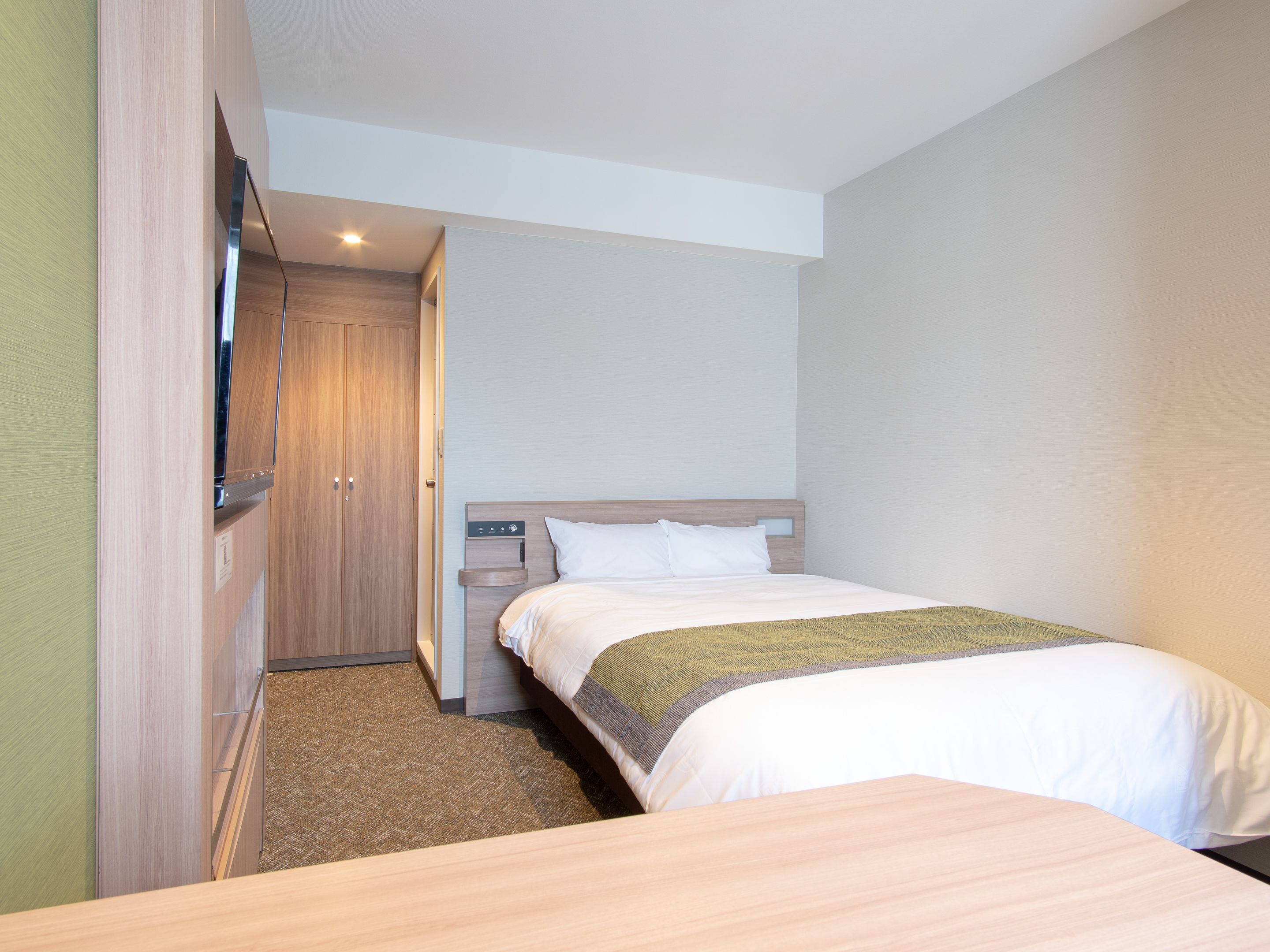Una habitación de hotel con cama, un armario de madera, una mesita de noche y un televisor montado en la pared.