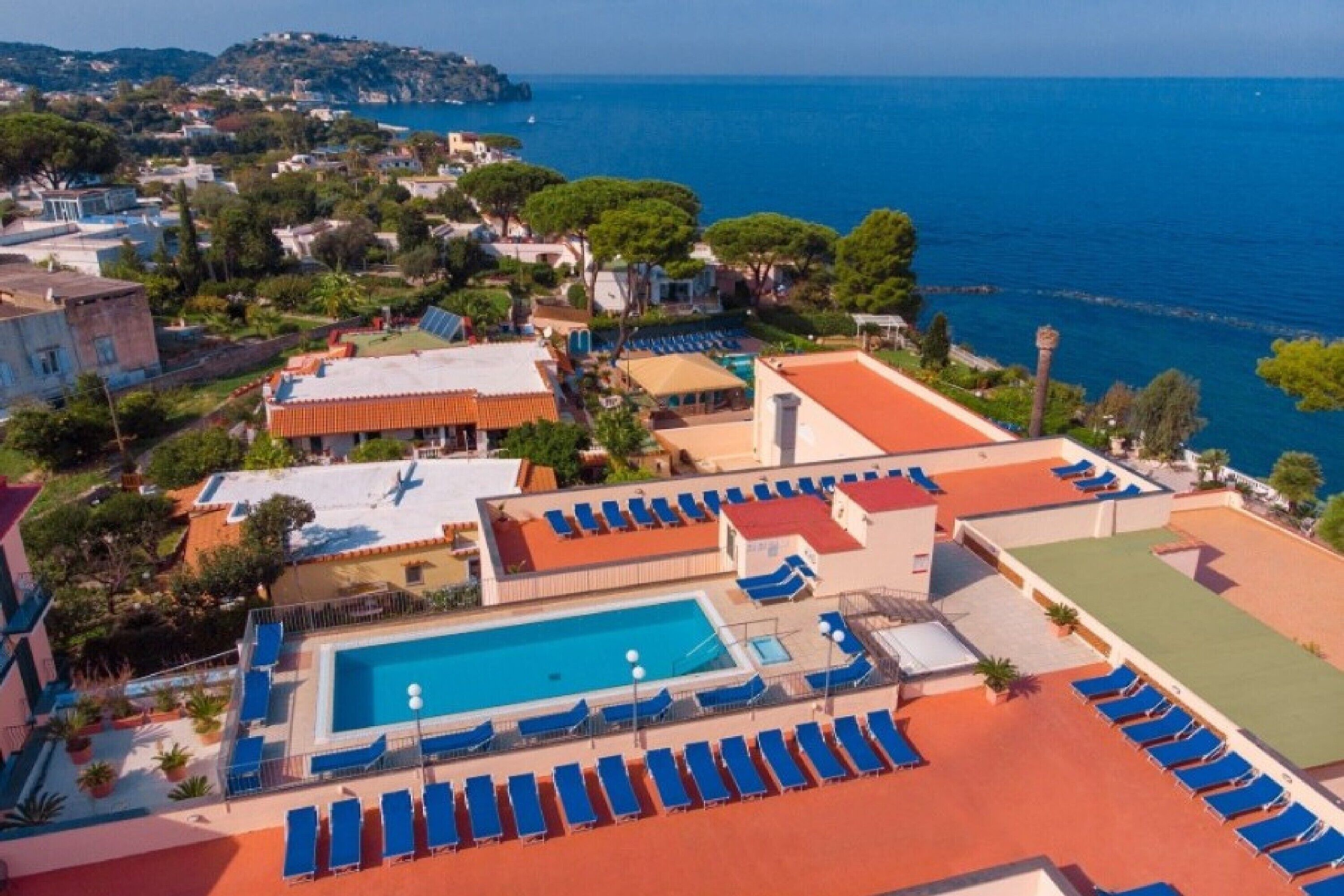 A resort with a swimming pool, sun loungers, and a view of the sea.